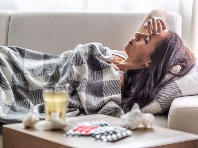 Frau liegt krank auf der Couch | © Getty Images/SimpleImages