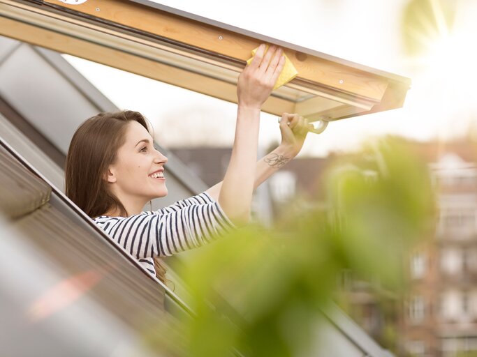 Eine junge Frau putzt die Fensterrahmen mit Waschmittel und einem Lappen | © GettyImages/Westend61