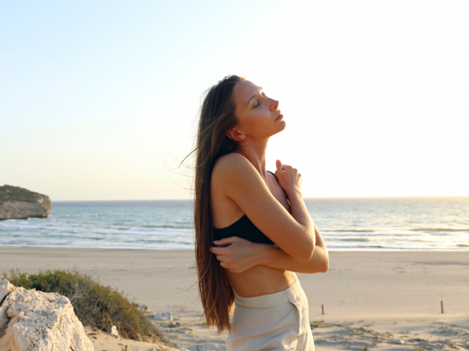 Frau am Strand umarmt sich selbst | © Getty Images/Westend61