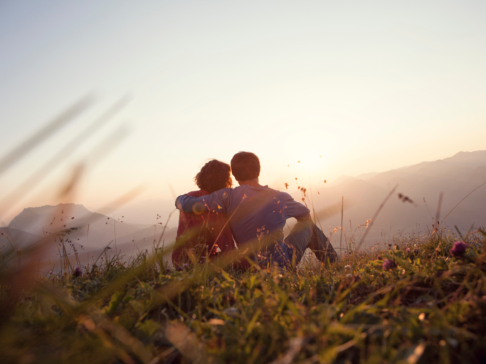 Frau und Mann sitzen auf Berg vor Sonnenuntergang | © Getty Images/Westend61