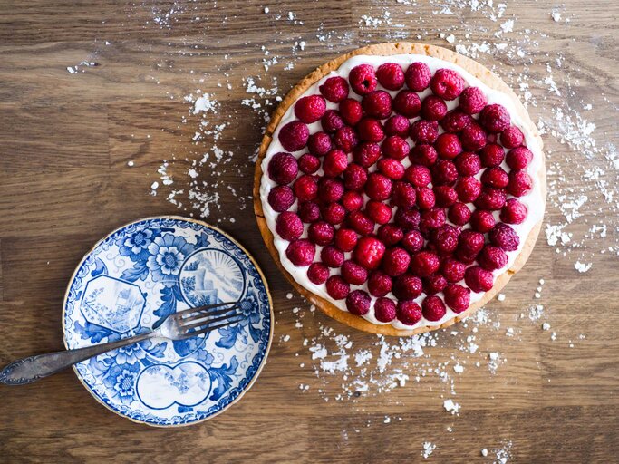 Ein Kuchenboden mit Schlagcreme bestrichen und mit Himbeeren belegt | © Getty Images/Jean-Luc Farges