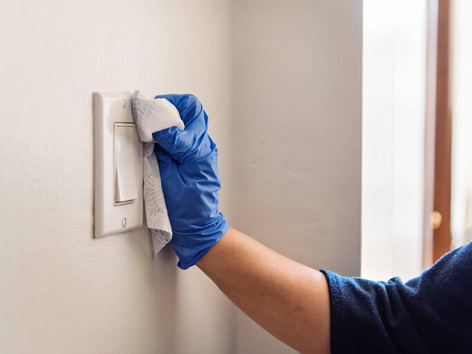 Hand in Nahaufnahme, die einen Putzhandschuh trägt und einen Lichtschalter reinigt | © Getty Images/martinedoucet