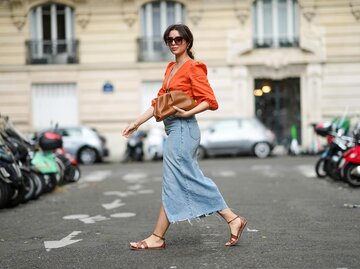 Streetstyle von Frau mit Jeansrock, oranger Bluse und braunen Sandalen | © Getty Images/Edward Berthelot