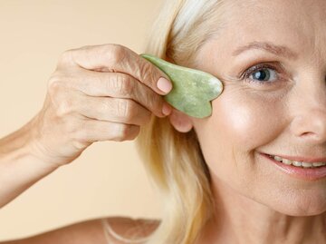 Reife Frau massiert ihr Gesicht mit Gua Sha Stein | © gettyimages.de/ creative credit