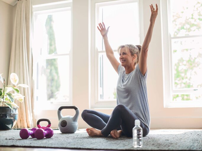 Frau sitzt im Wohnzimmer auf der Yogamatte und übt Sport.  | © iStock | Stígur Már Karlsson /Heimsmyndir