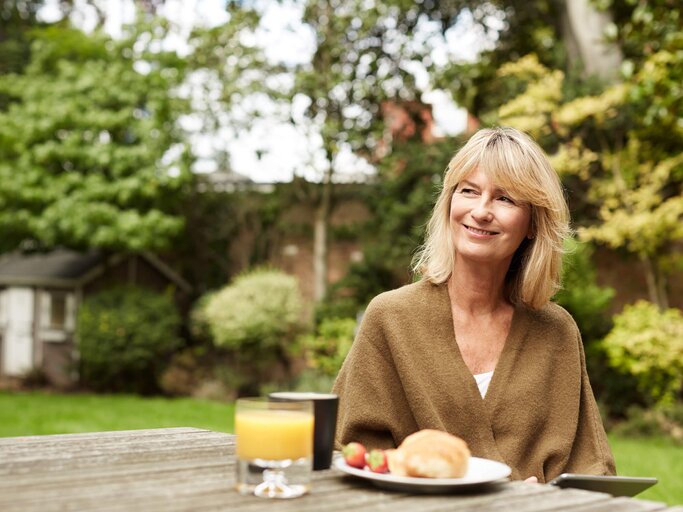 Gesund Frau sitzt beim Frühstück im Garten und hält ein Tablet in der Hand. | © iStock.de / kupicoo