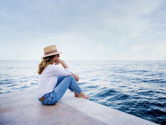 Frau sitzt in Jeans am Meer | © Getty Images/	Szepy