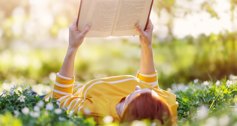 Frau liest Buch in frühlingshafter Blumenwiese | © GettyImages/LeManna