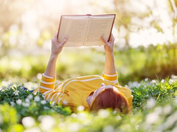 Frau liest Buch in frühlingshafter Blumenwiese | © GettyImages/LeManna